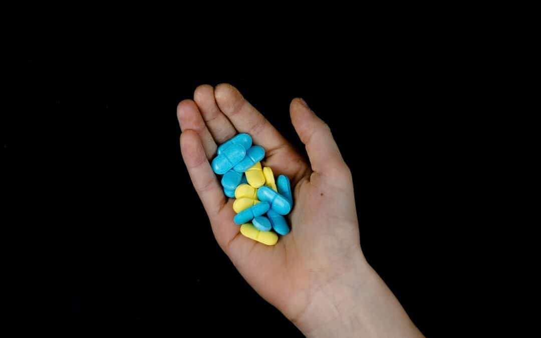 hand holding yellow and blue pills on black background