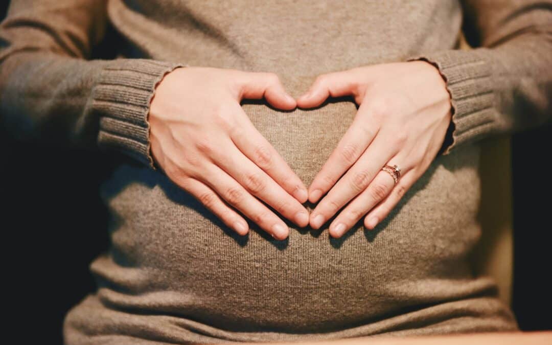 woman with hands in a heart shape on her pregnant belly