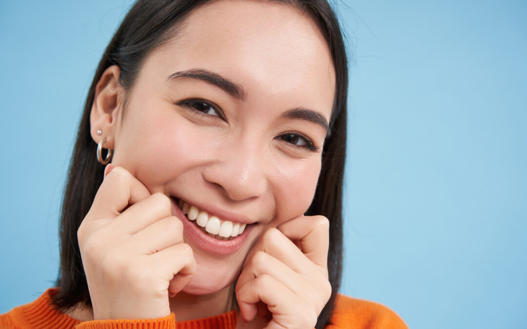 close up of woman pinching her cheeks and smiling on blue background